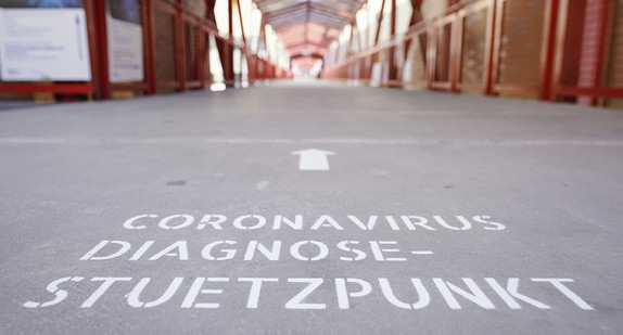 Auf dem Boden eines überdachten Zugangswegs zum Universitätsklinikum ist der Schriftzug „Coronavirus Diagnose-Stuetzpunkt“ angebracht.